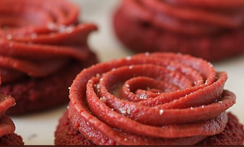 A plate of Red Velvet Blossoms with vibrant red cookies topped with shiny chocolate kisses, surrounded by a festive holiday setting